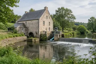 Ancien moulin en pierre au bord d’une rivière de Mayenne ou de Sarthe, équipé d’une petite installation hydroélectrique intégrée au site.